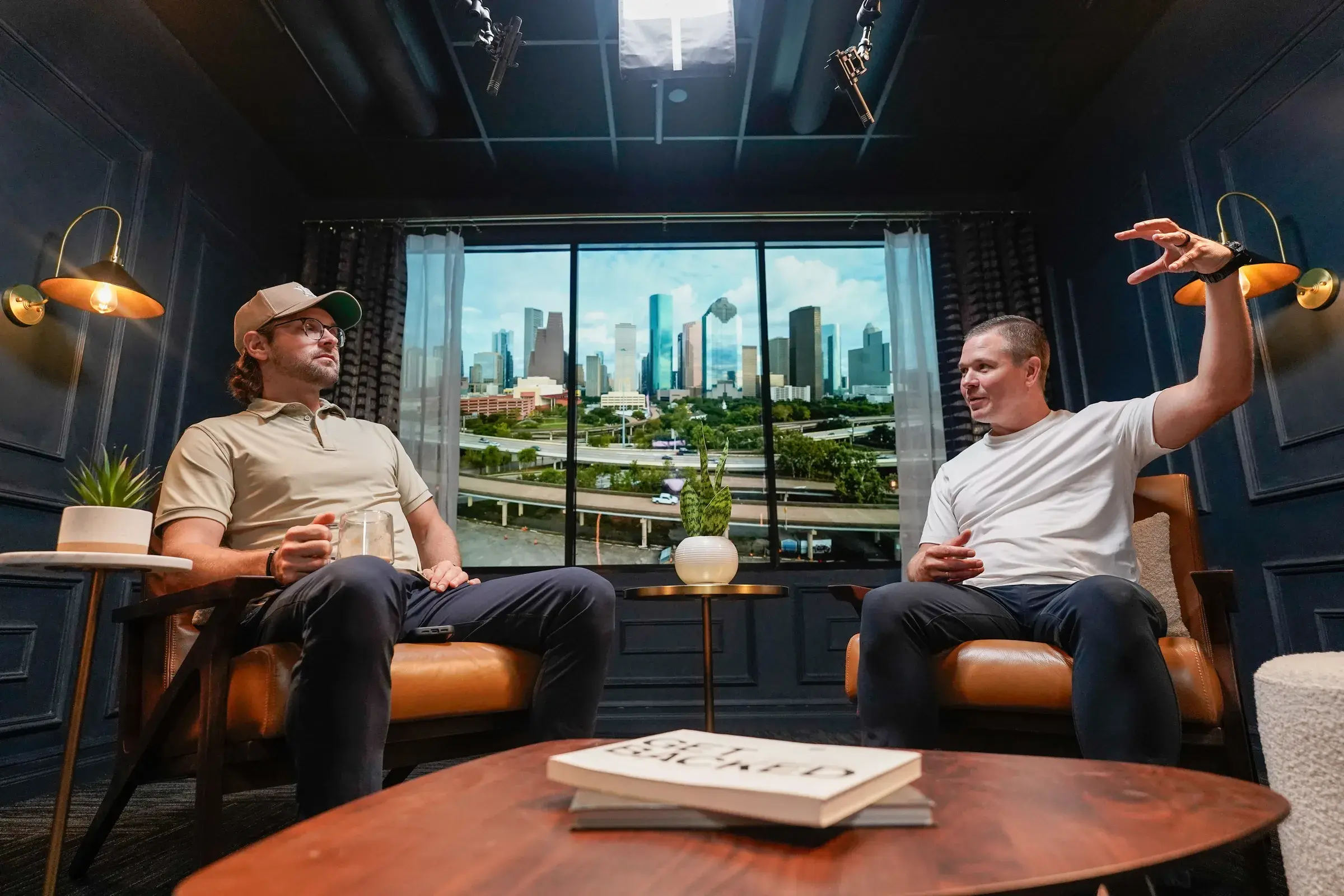 Two people mid-conversation in the finished studio, seated in the leather chairs with the skyline behind them