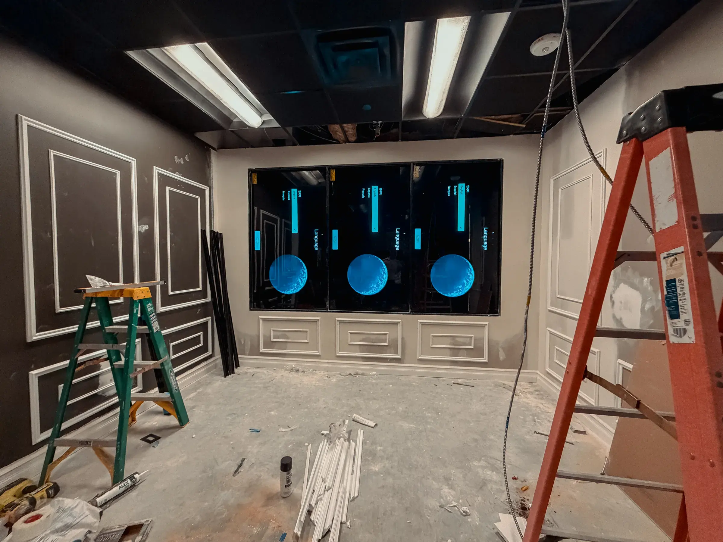 The faux window mid-construction — three large displays mounted in the wall opening showing setup screens, the surrounding panel molding installed but unfinished
