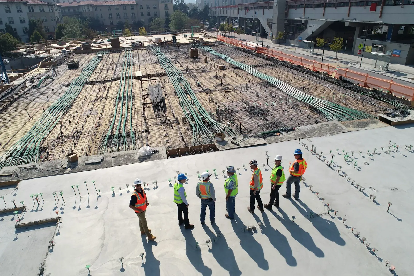 A crew of hard-hatted workers standing together on a concrete slab above a rebar foundation
