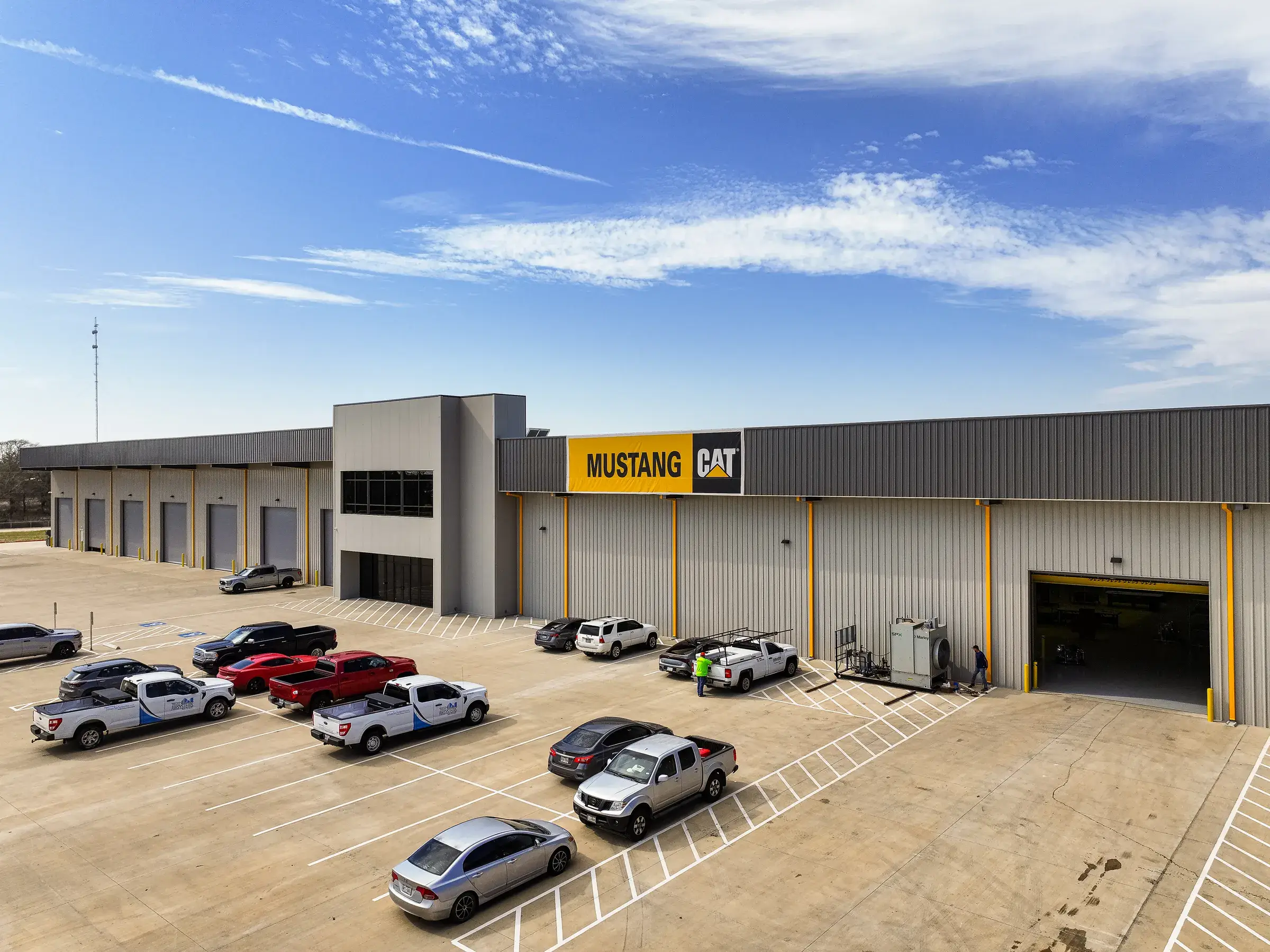 The front of the Mustang CAT Hempstead facility — the yellow MUSTANG CAT sign over a row of service bays, with a full parking lot in front