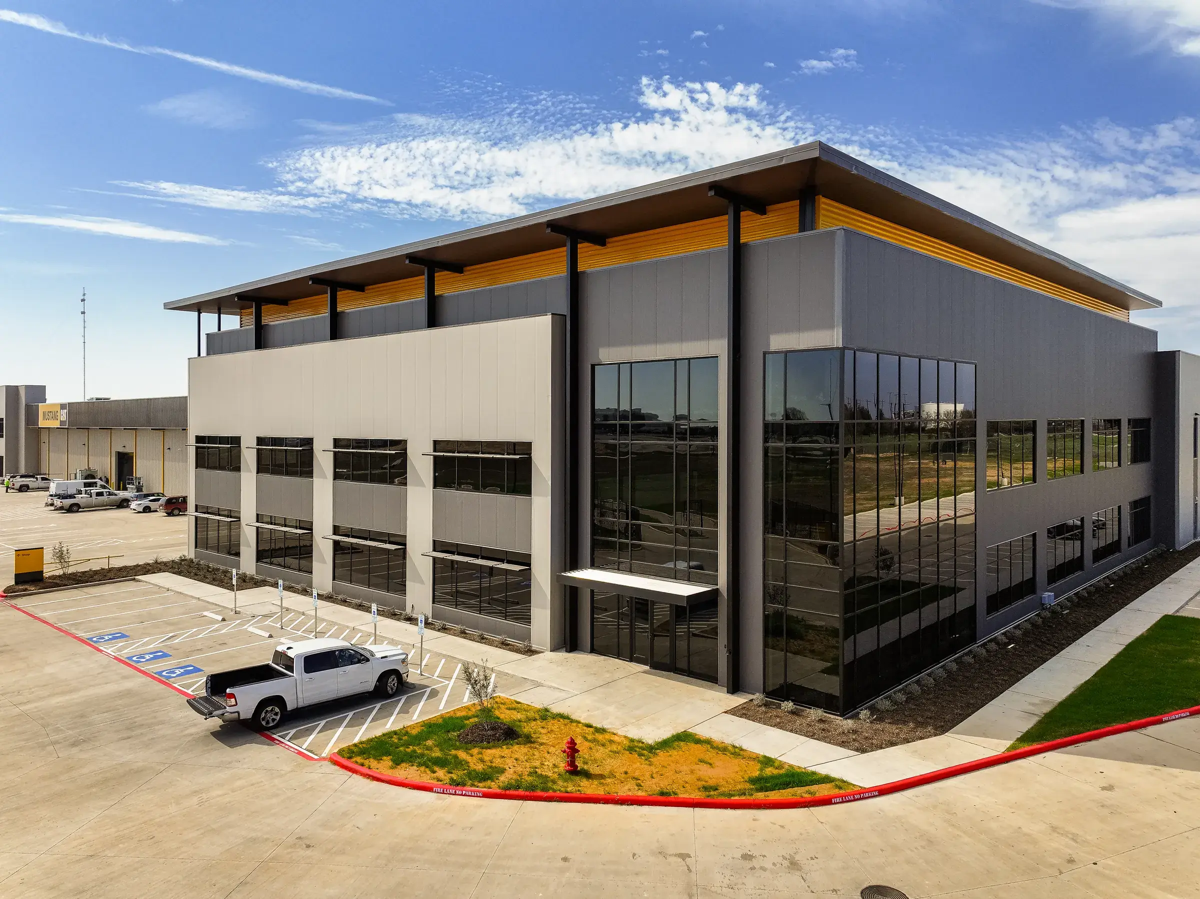 The two-story administrative block at the Mustang CAT Hempstead facility, dark glass set under a deep metal canopy