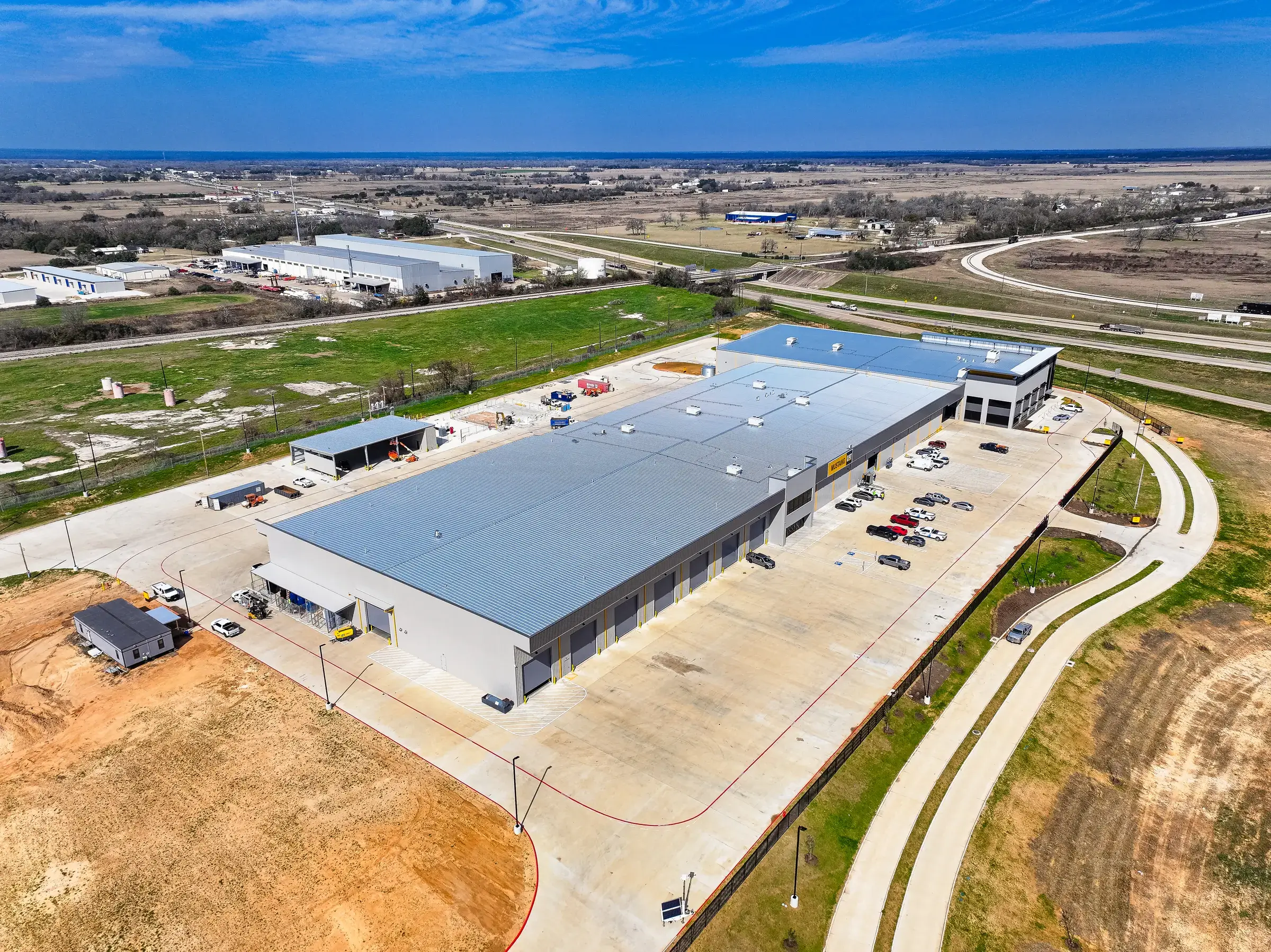 Aerial view of the completed Mustang CAT Hempstead facility — a long metal-clad service building with drive-through bays, paved yard, and administrative block
