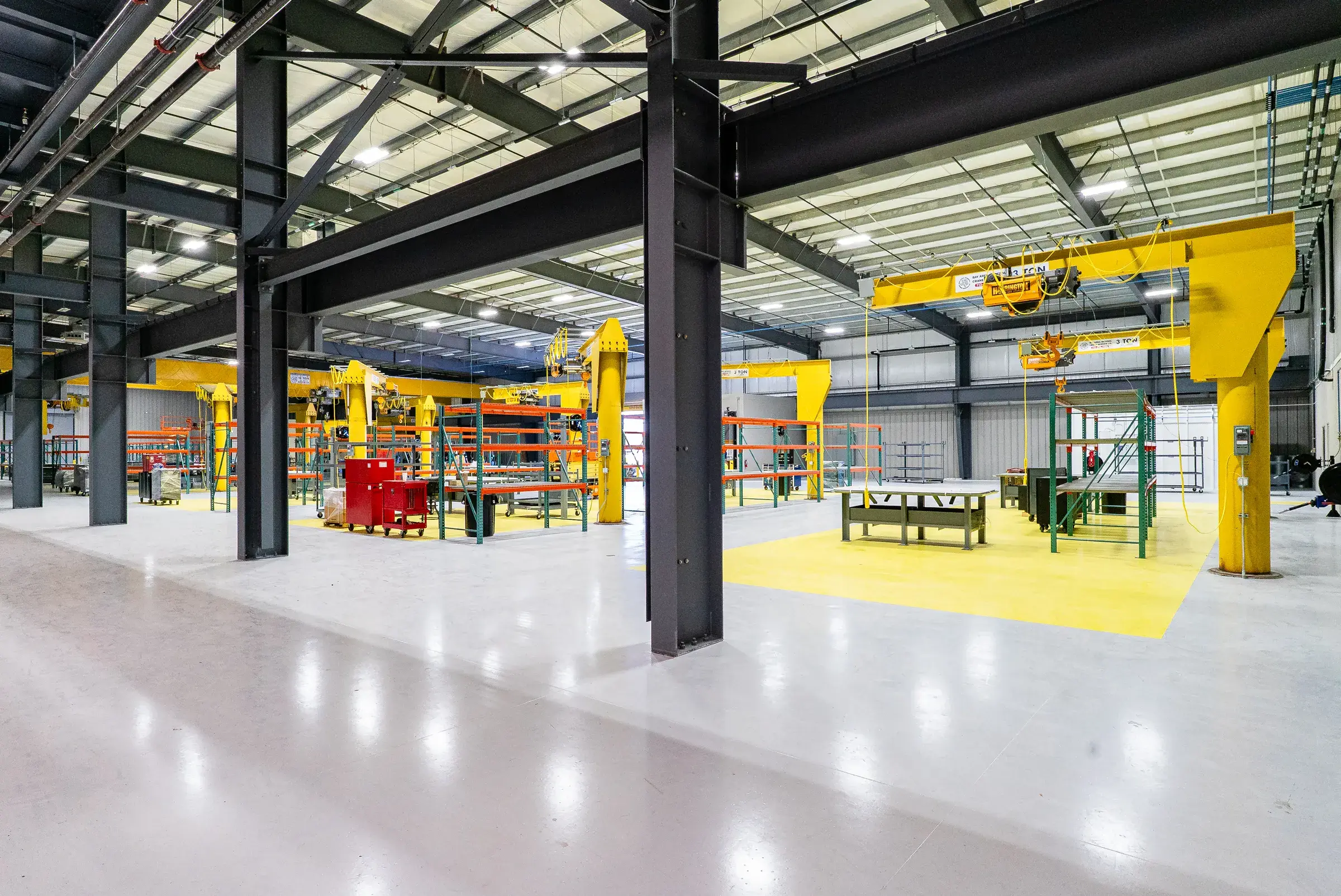 A rebuild bay on the shop floor with column-mounted yellow jib cranes over a striped epoxy work zone