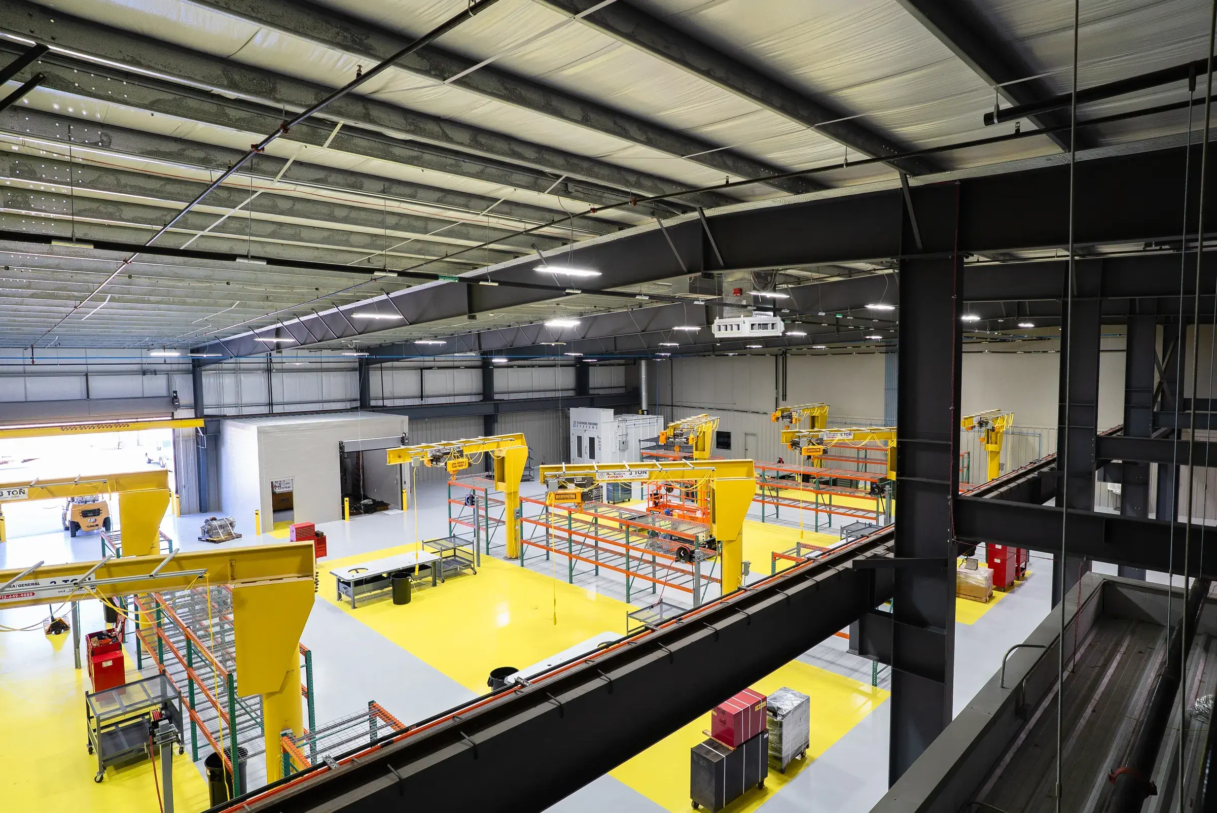 View from the office mezzanine down onto the shop floor, yellow jib cranes and marked work bays below