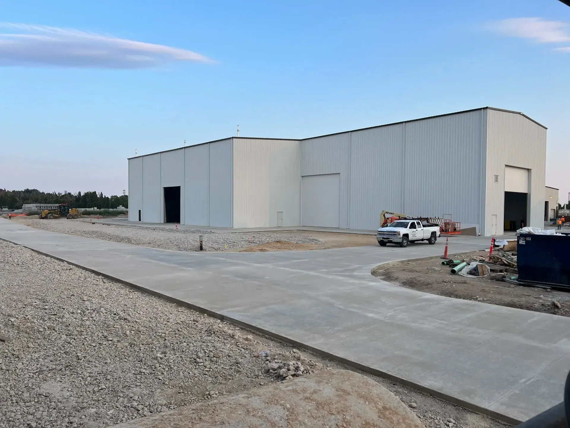 The completed Idaho Precast plant — a long metal-clad production building with tall drive-through bay doors, fronted by new concrete paving