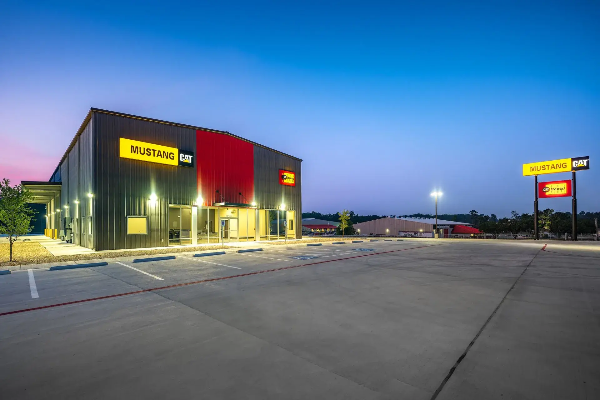 The finished Mustang CAT dealership and rental store at dusk, lit signage over a fresh parking lot