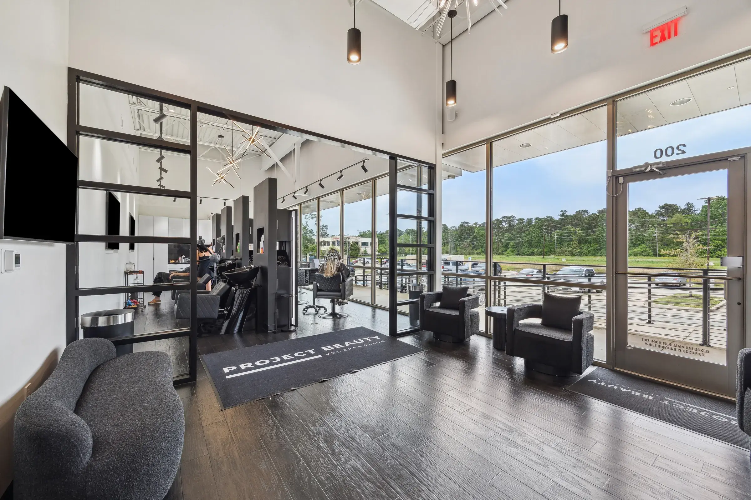The finished salon floor — styling stations set along a full-height window wall under black-framed partitions and exposed ceiling