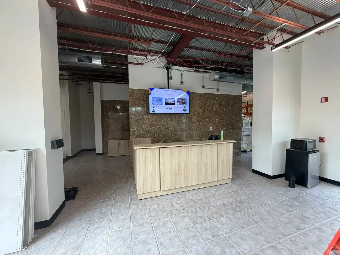 The finished SiTech reception area — a light wood front desk against a stone-clad wall with a wall-mounted display, under an exposed structural ceiling with linear lighting