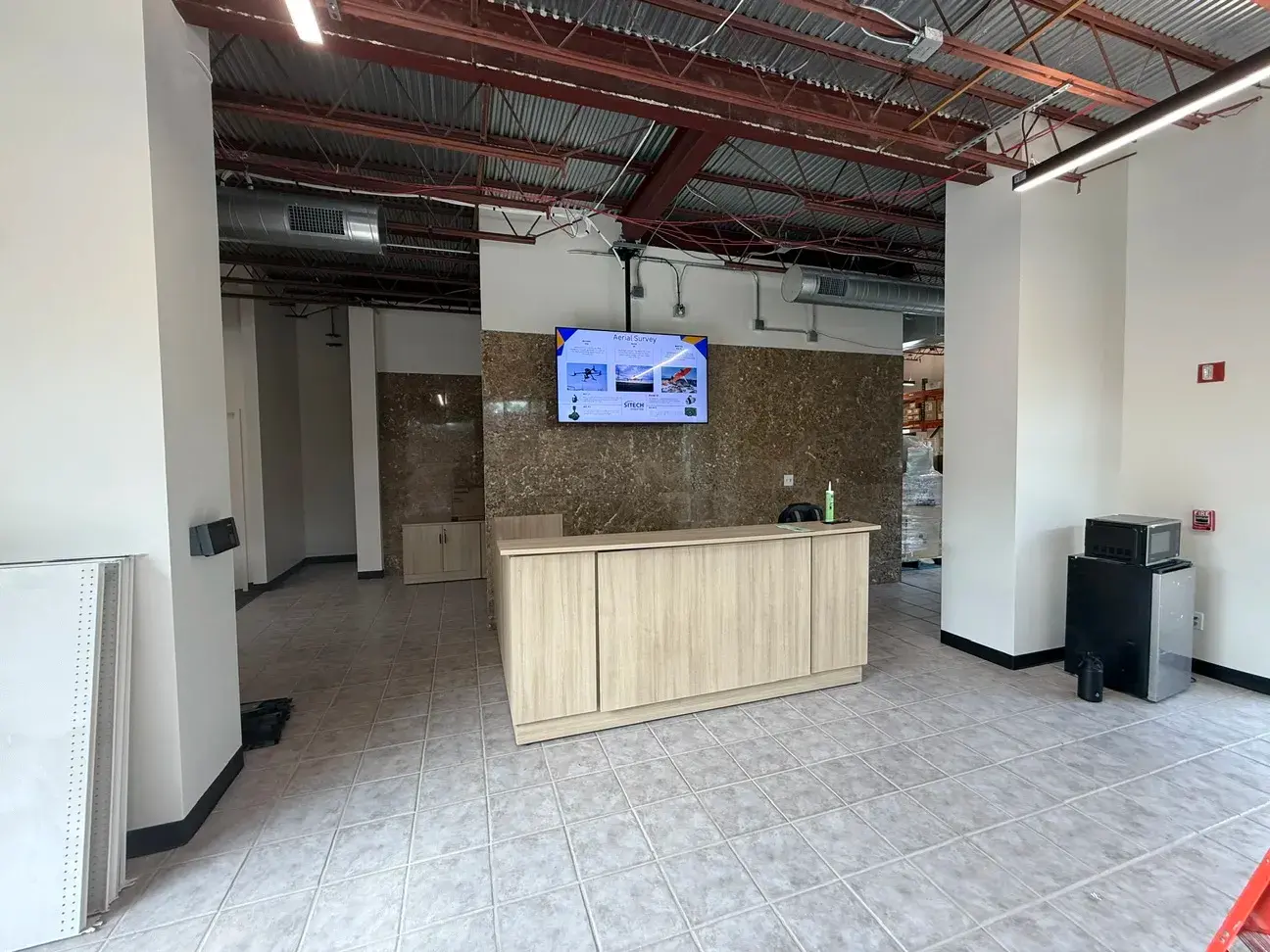 The finished SiTech reception area — a light wood front desk against a stone-clad wall with a wall-mounted display, under an exposed structural ceiling with linear lighting