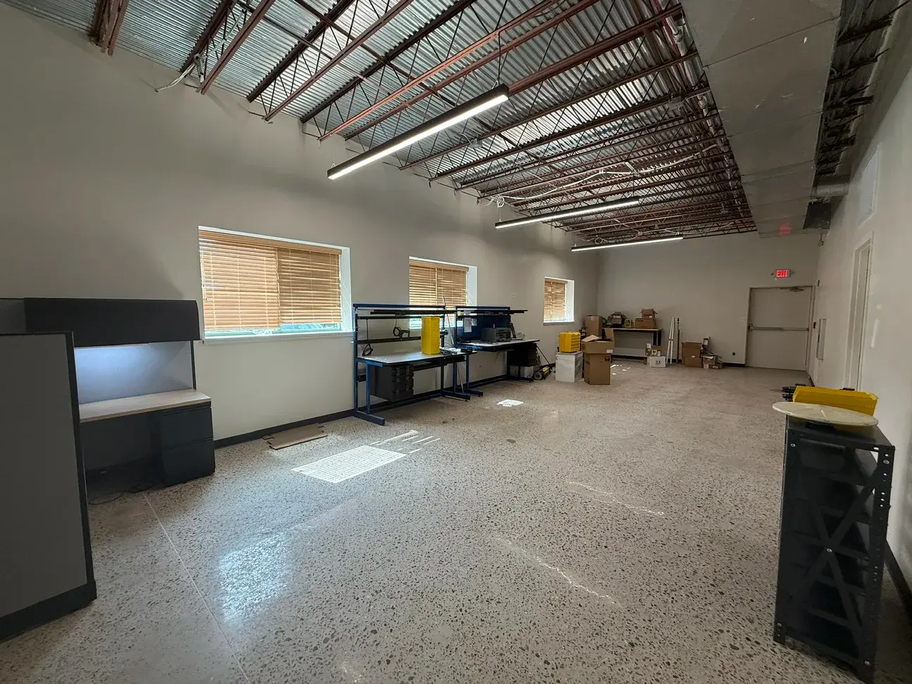 An open work area with polished concrete floors, daylight from window openings, and new linear fixtures hung below the exposed roof structure