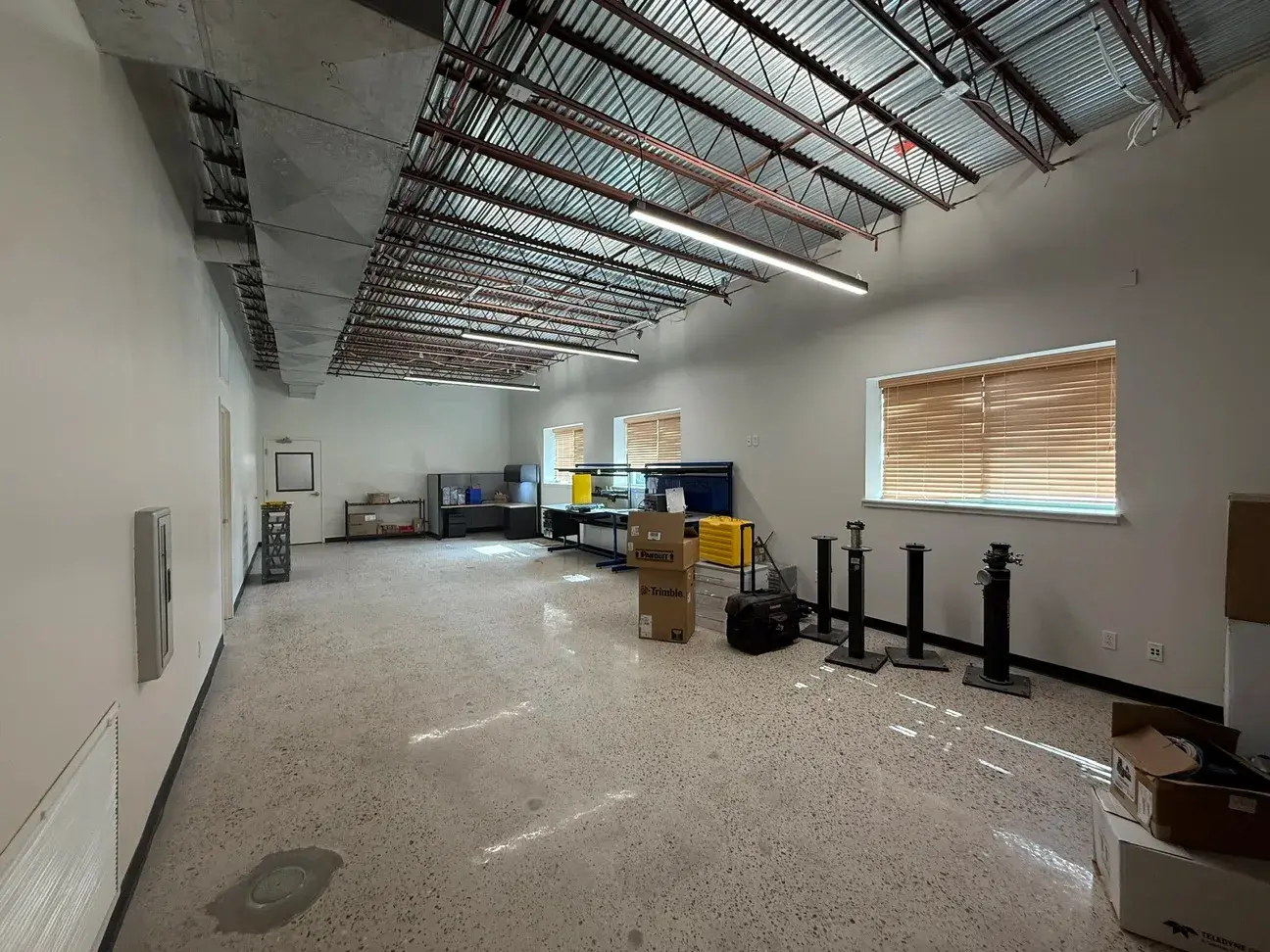 A second open area running the depth of the building, exposed structure and ductwork overhead, lit end to end by the new fixtures